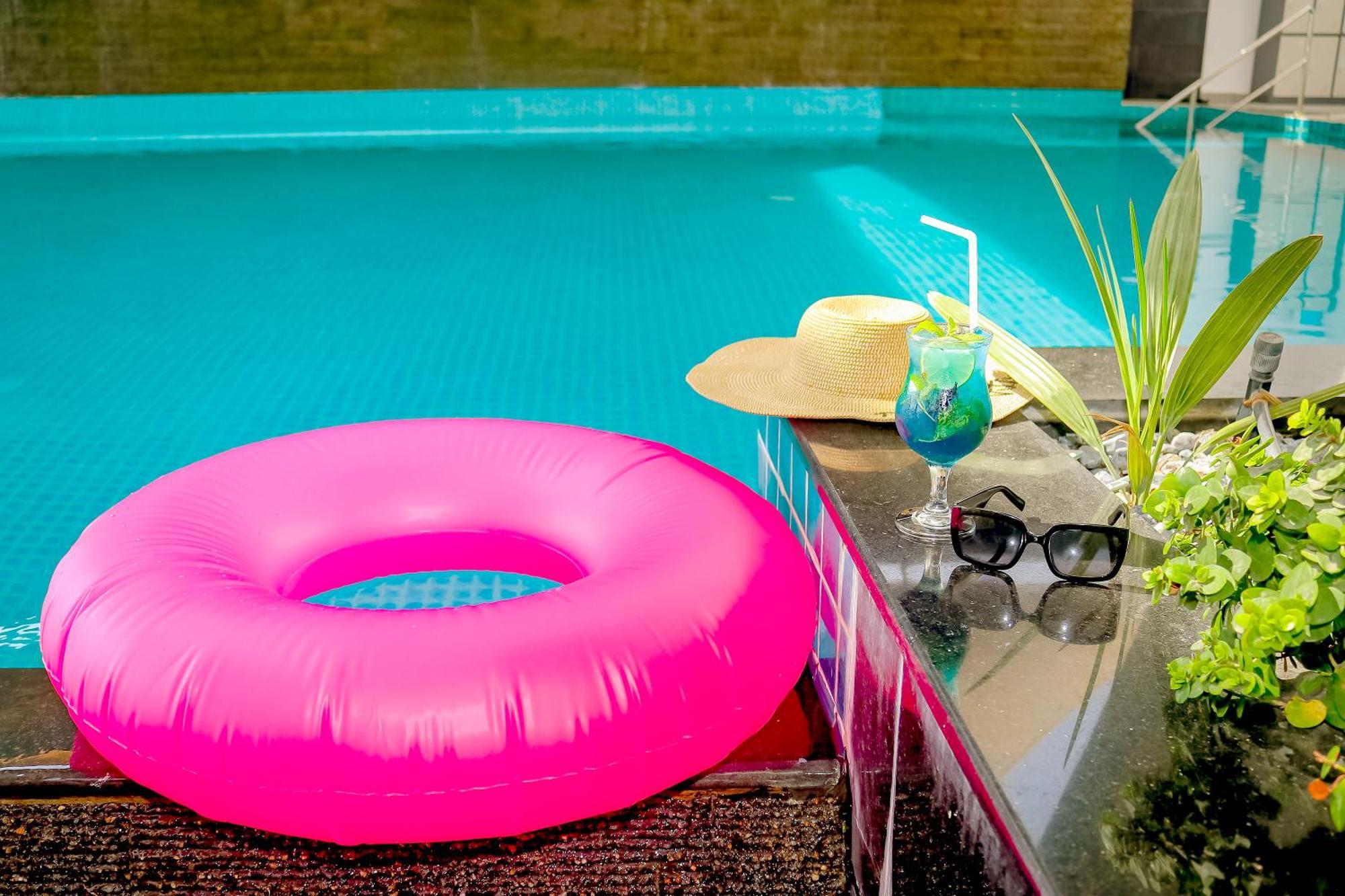 ลากูนา บีช ลักซัวรี รีสอร์ต แอนด์ สปา Hotel มานามา ภายนอก รูปภาพ The photo shows a vibrant and inviting scene by a swimming pool. In the foreground, there is a large pink inflatable float and a stylish straw hat. Next to the float, a refreshing cocktail in a glass is displayed, complete with a straw and garnishes.