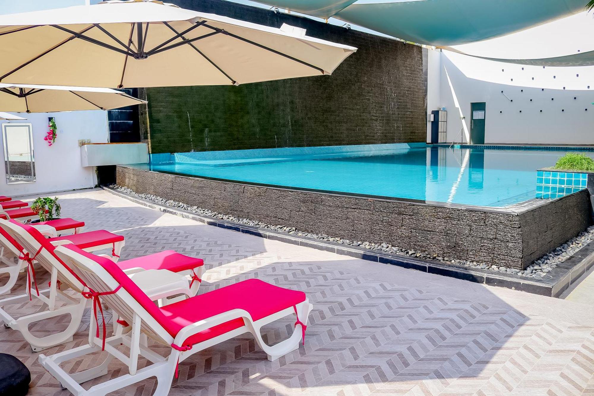 ลากูนา บีช ลักซัวรี รีสอร์ต แอนด์ สปา Hotel มานามา ภายนอก รูปภาพ The photo shows a pool area featuring a rectangular swimming pool with clear blue water. Surrounding the pool are light-colored lounge chairs with pink cushions, positioned under large umbrellas for shade. The pool is bordered by a textured wall, and