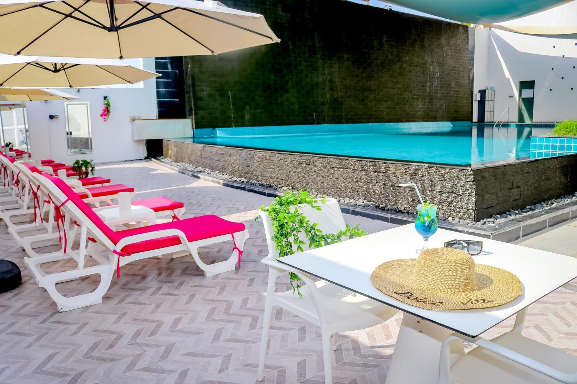 ลากูนา บีช ลักซัวรี รีสอร์ต แอนด์ สปา Hotel มานามา ภายนอก รูปภาพ The photo shows a sunny poolside area with bright red lounge chairs arranged neatly beside a swimming pool. There are large beige umbrellas providing shade. A small table is set up with a straw hat and a colorful drink, suggesting a relaxed, tropical