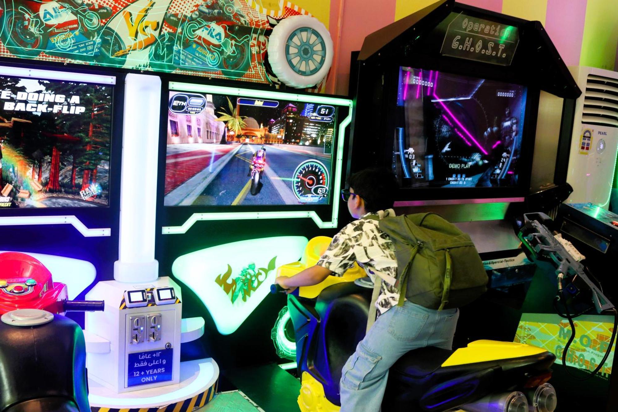ลากูนา บีช ลักซัวรี รีสอร์ต แอนด์ สปา Hotel มานามา ภายนอก รูปภาพ The photo shows a person playing an arcade motorcycle racing game. They are seated on a motorcycle-shaped seat, actively engaging with the game displayed on the screen in front of them. The screen shows a vibrant racing scene with streets and colorfu