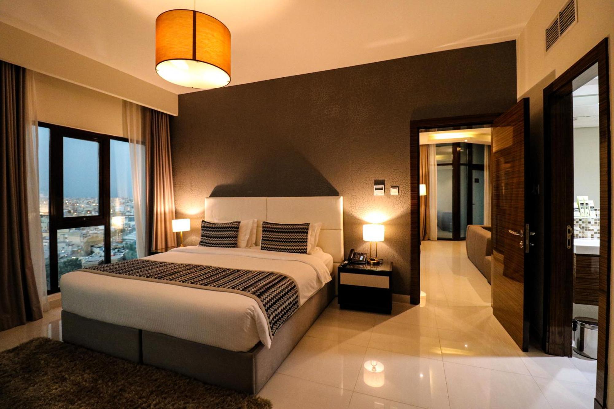 ลากูนา บีช ลักซัวรี รีสอร์ต แอนด์ สปา Hotel มานามา ภายนอก รูปภาพ The photo depicts a modern hotel room or suite. It features a large bed with a white and gray color scheme, accented with decorative pillows. On either side of the bed, there are sleek bedside lamps providing warm lighting. The walls are a dark color