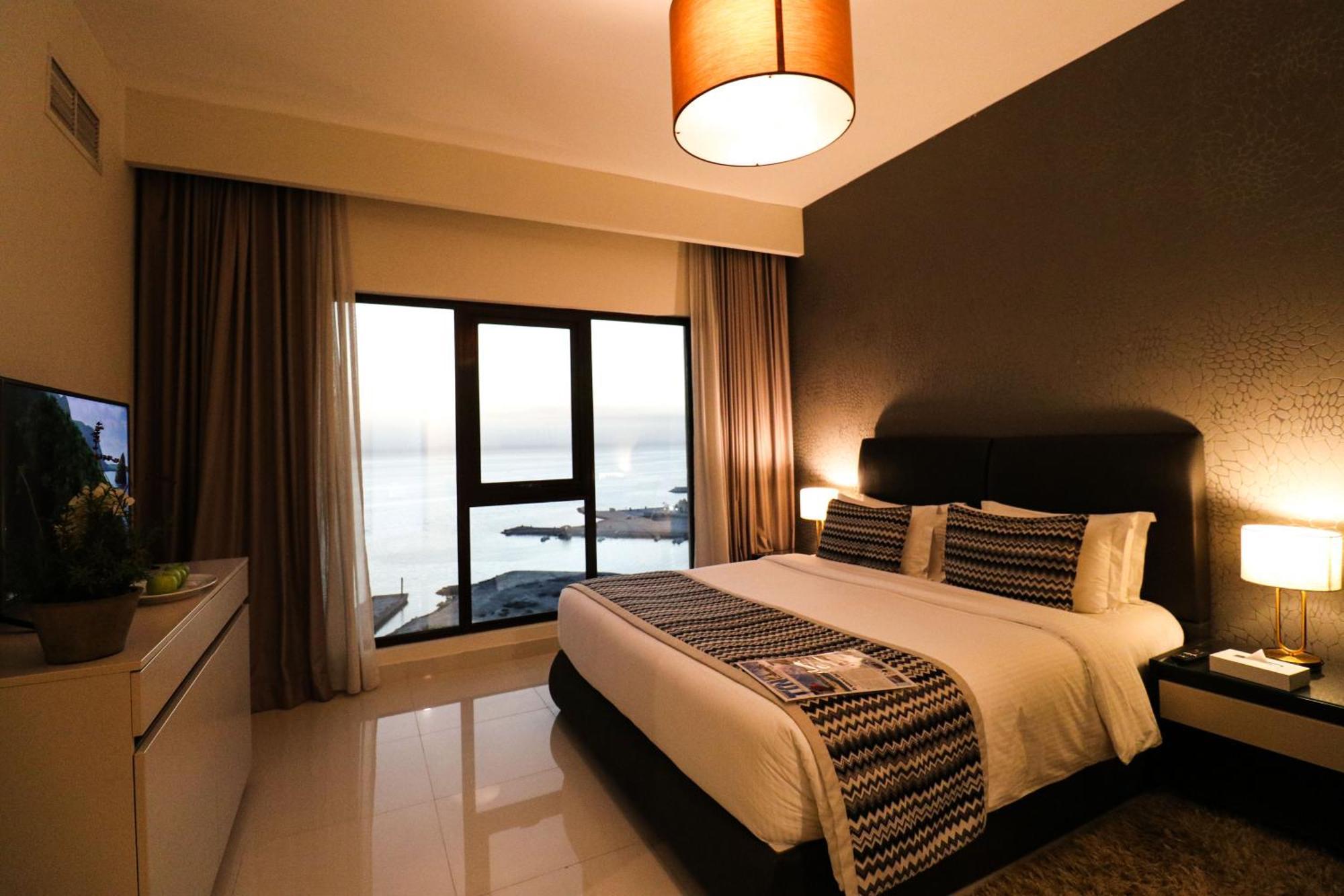 ลากูนา บีช ลักซัวรี รีสอร์ต แอนด์ สปา Hotel มานามา ภายนอก รูปภาพ The photo shows a modern hotel room featuring a neatly made bed with decorative pillows. The room has a stylish design with a dark accent wall and a large window that offers a view of the outdoors. Natural light comes in, giving the space a bright an