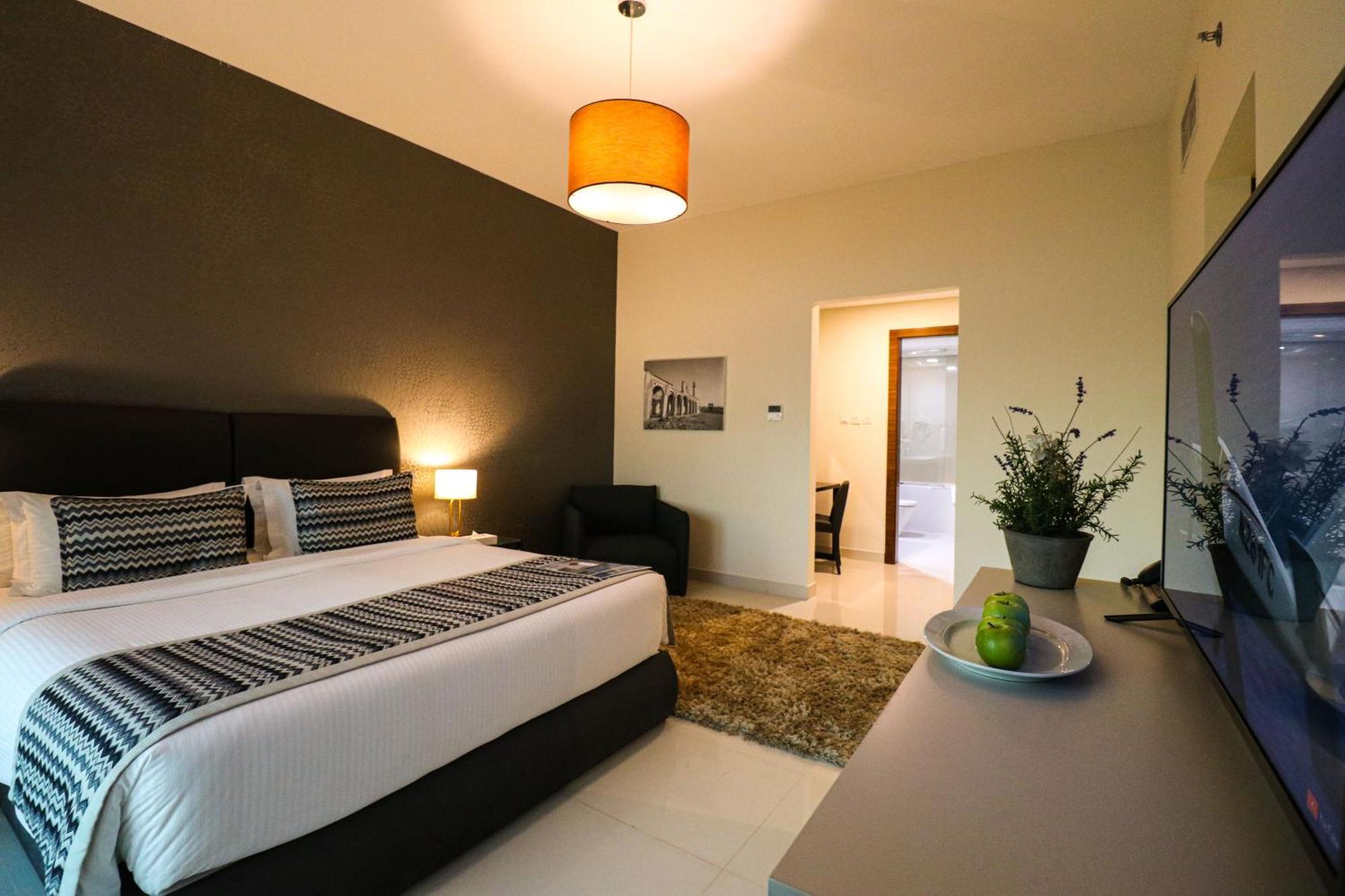 ลากูนา บีช ลักซัวรี รีสอร์ต แอนด์ สปา Hotel มานามา ภายนอก รูปภาพ The photo shows a modern hotel room. It features a large bed with a neatly made white and dark-colored duvet. On either side of the bed, there are bedside tables with lamps. The wall behind the bed is painted in a dark color, creating a contrast with
