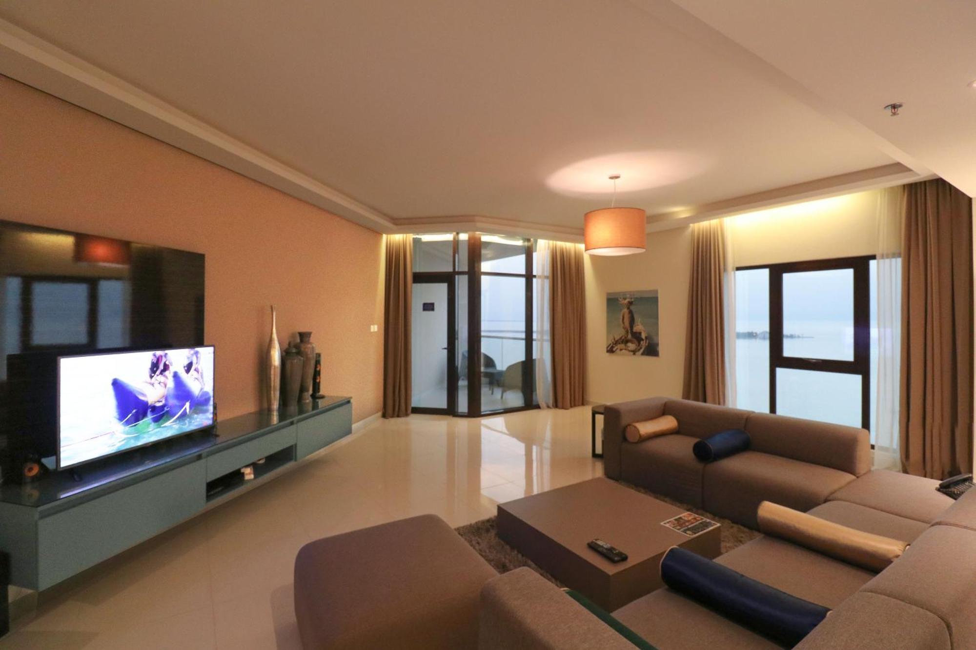 ลากูนา บีช ลักซัวรี รีสอร์ต แอนด์ สปา Hotel มานามา ภายนอก รูปภาพ The photo shows a modern living room with a sleek design. There is a large wall-mounted television on a contemporary entertainment unit, with decorative items placed beside it. The room features a comfortable sectional sofa in light tones, with a cof