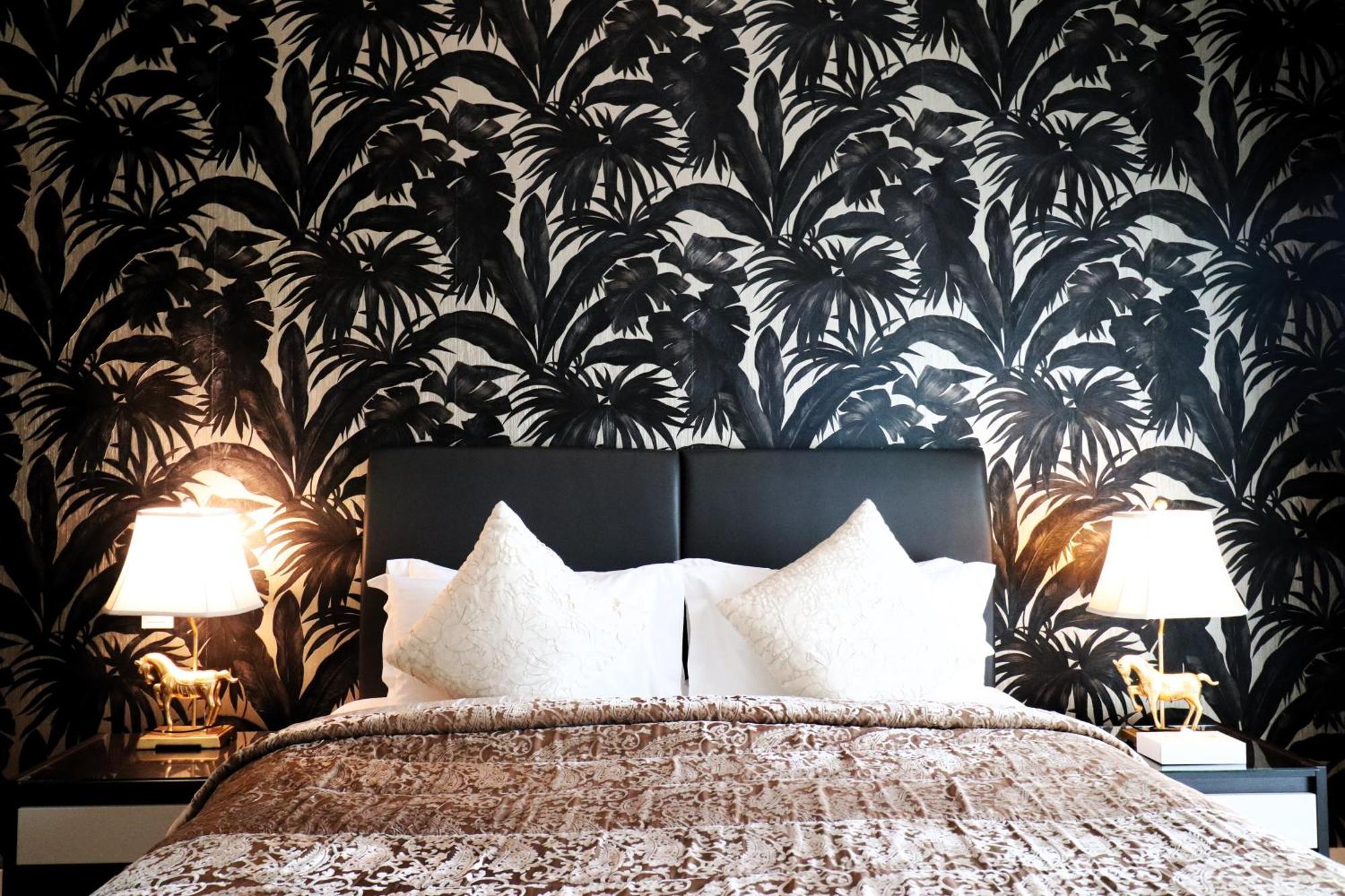 ลากูนา บีช ลักซัวรี รีสอร์ต แอนด์ สปา Hotel มานามา ภายนอก รูปภาพ The photo depicts a stylish bedroom featuring a distinctive wall covered in a black and white tropical foliage wallpaper. The bed has a modern black headboard and is adorned with white pillows, creating a clean and elegant look. A textured brown thro