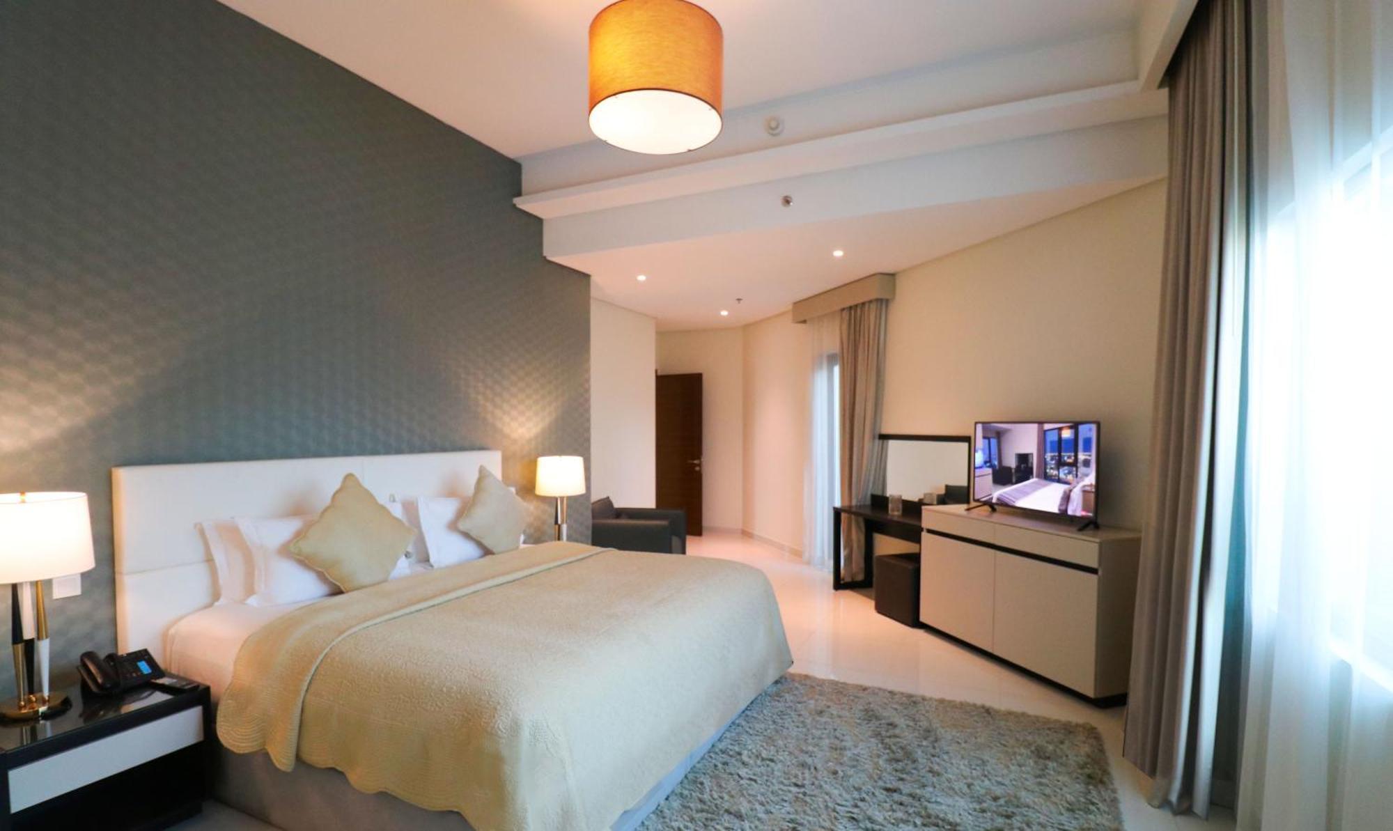 ลากูนา บีช ลักซัวรี รีสอร์ต แอนด์ สปา Hotel มานามา ภายนอก รูปภาพ The photo shows a modern hotel room featuring a large bed with a light-colored blanket and decorative pillows. The walls are painted in a subtle shade, and there is a textured accent wall behind the bed. On one side, a bedside lamp provides warm ligh