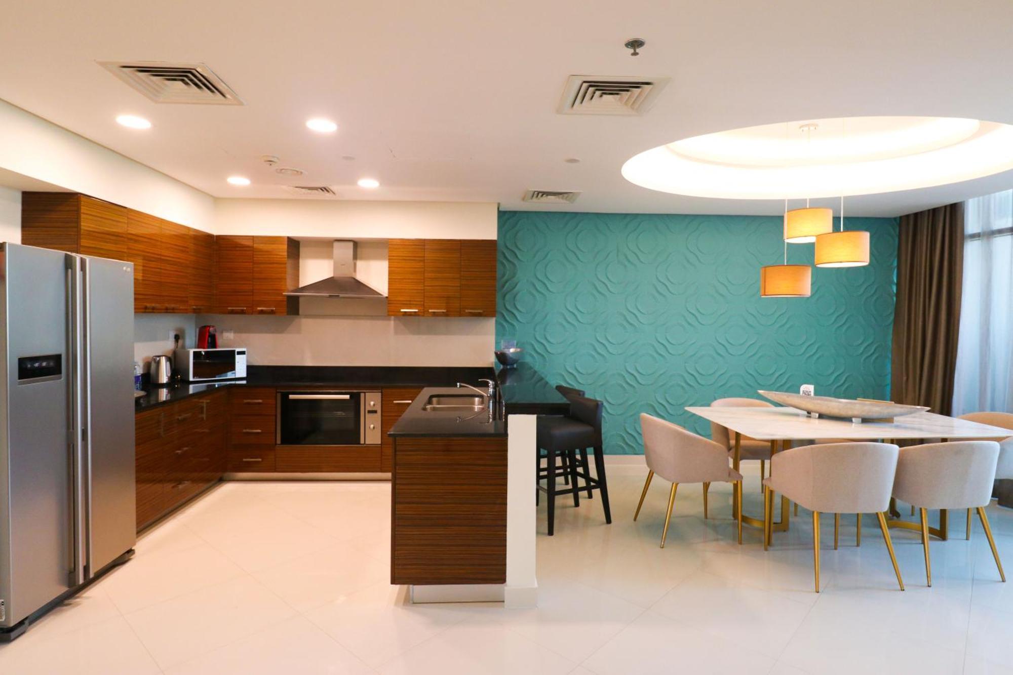 ลากูนา บีช ลักซัวรี รีสอร์ต แอนด์ สปา Hotel มานามา ภายนอก รูปภาพ The photo shows a modern kitchen and dining area. The kitchen features wooden cabinets, sleek appliances including a stainless steel refrigerator, microwave, and an oven. There is a dark countertop and a small breakfast bar with high stools. The wall